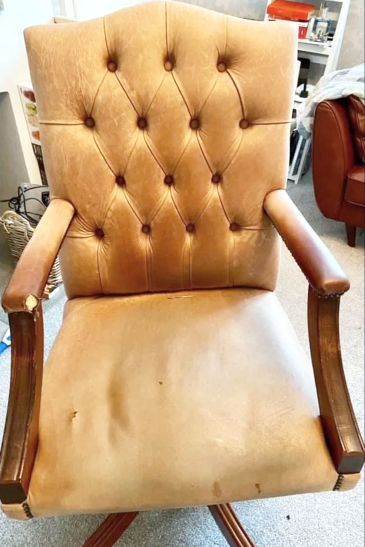 A vintage-style beige upholstered armchair with a tufted backrest and wooden arm supports, showing signs of wear and tear.