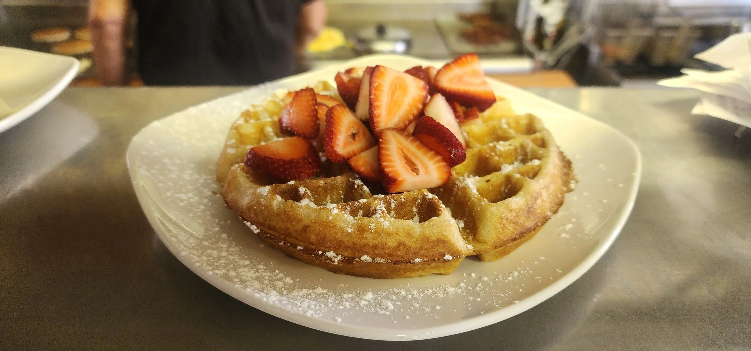 A plate of a Belgian waffle topped with fresh strawberries and powdered sugar.