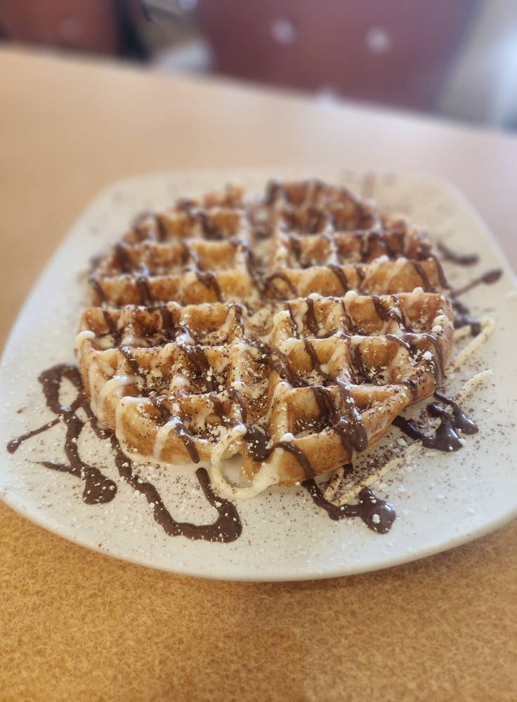 Plate of waffles topped with chocolate and white sauces, sprinkled with powdered sugar.