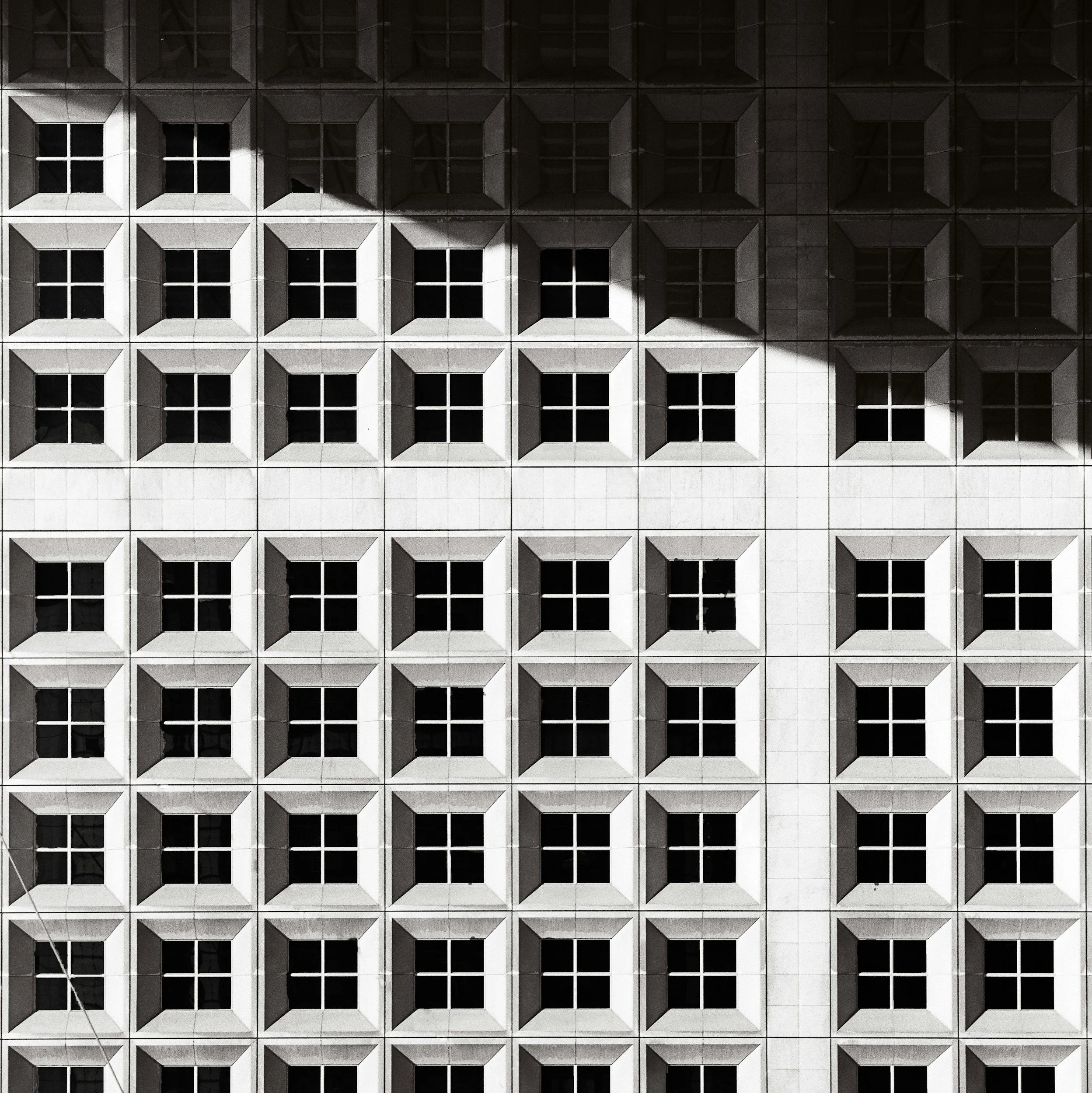 A grid of window-like structures on a building with shadows cast on it.