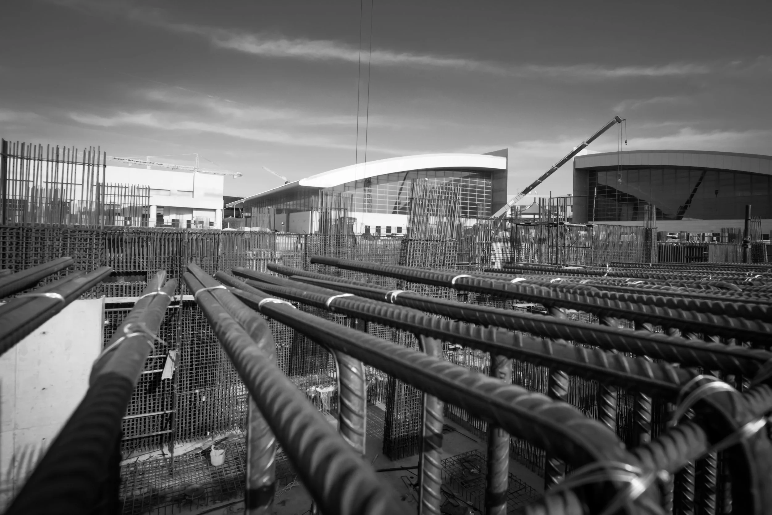 Under construction site with metal rebar framework and buildings in the background under a cloudy sky.