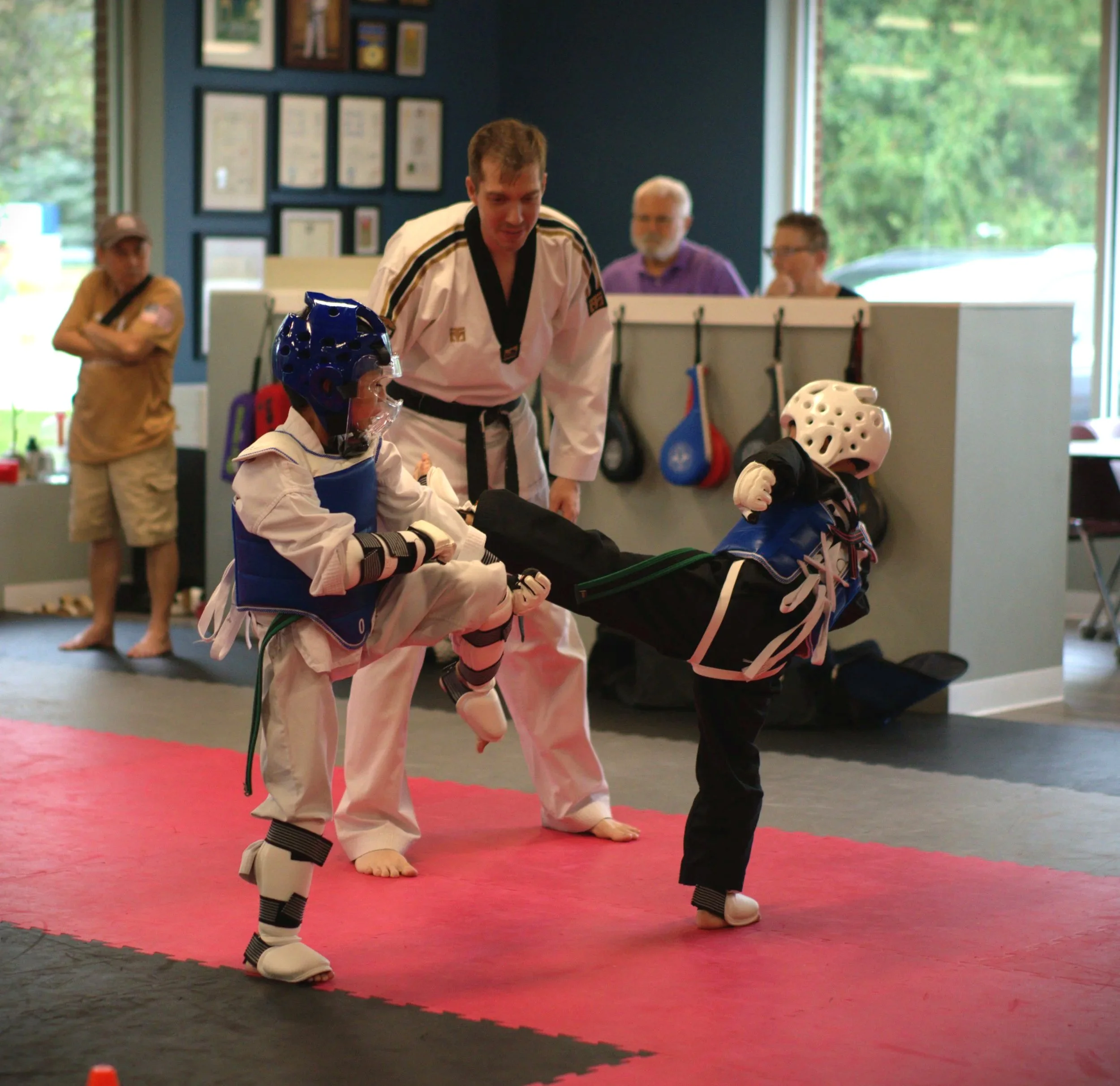 Martial arts instructor teaches young students in a dojo, with a focus on a boy wearing a helmet and protective gear.