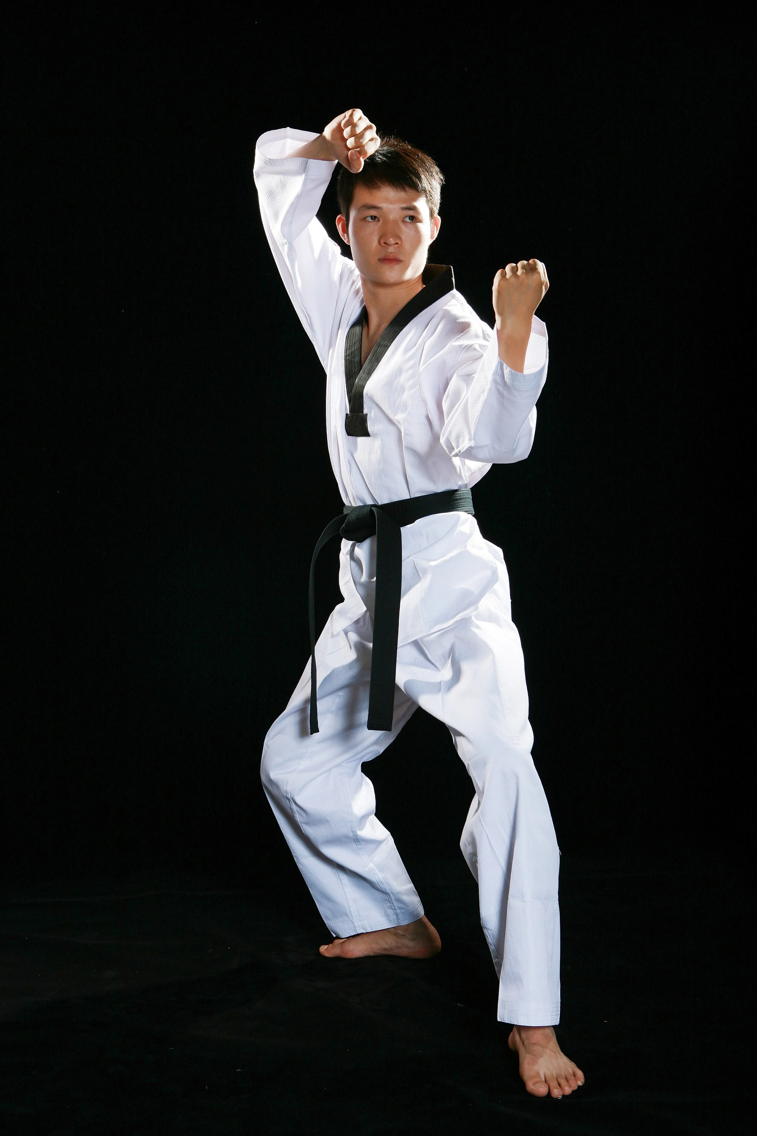 A martial artist in a white gi with a black belt practicing a karate punch against a black background.