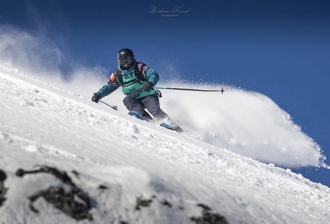 A child skiing down a snowy mountain slope against a clear blue sky.