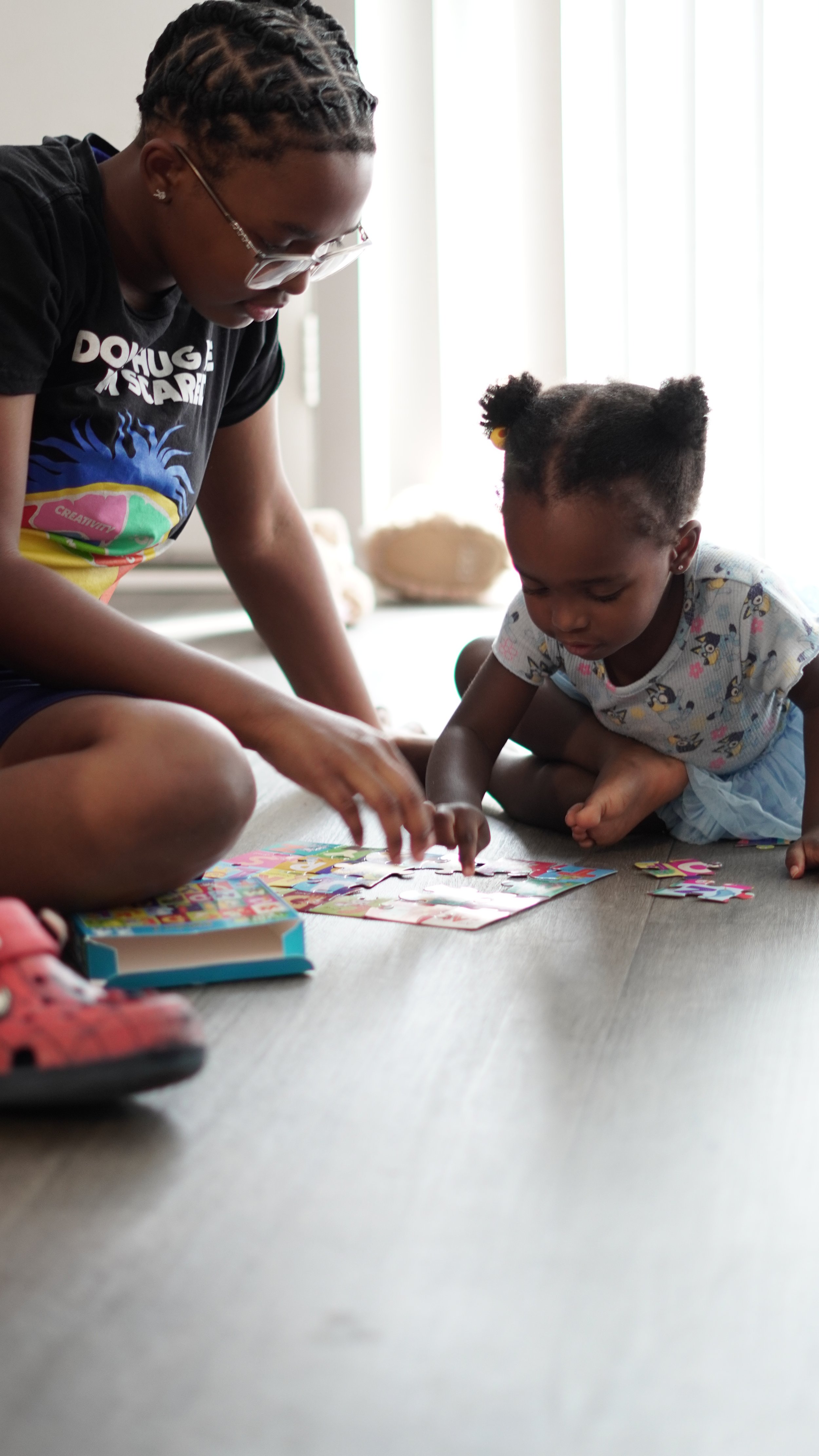 A woman and a young girl are sitting on the floor assembling a colorful jigsaw puzzle.