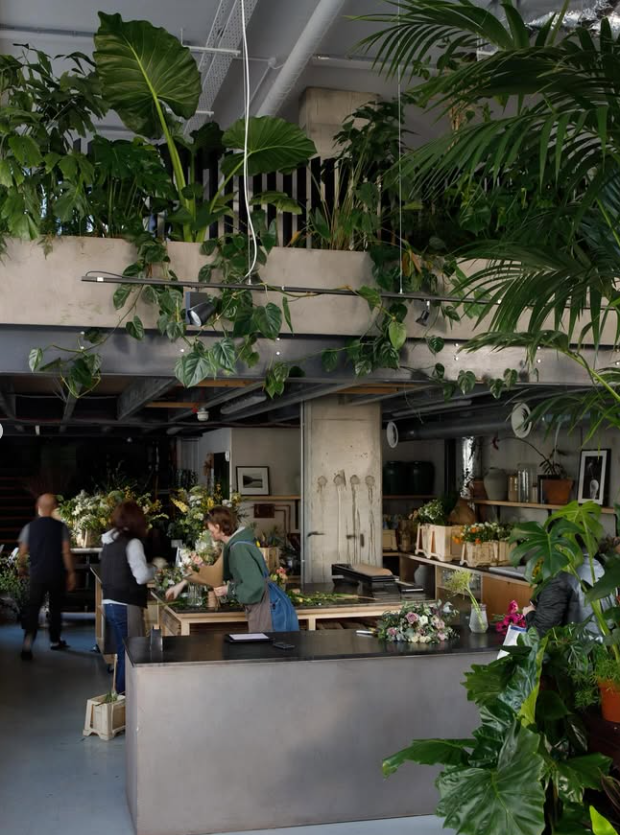 People working on flower arrangements in a flower shop surrounded by various potted plants and floral displays.