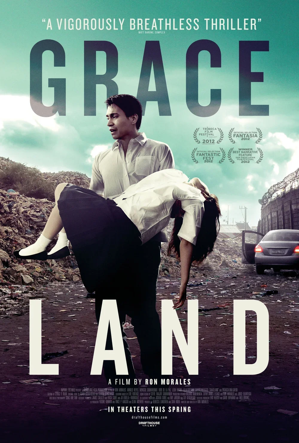 Movie poster for 'Grace Land,' showing a man carrying an unconscious woman in a trash-strewn outdoor area with an overcast sky.