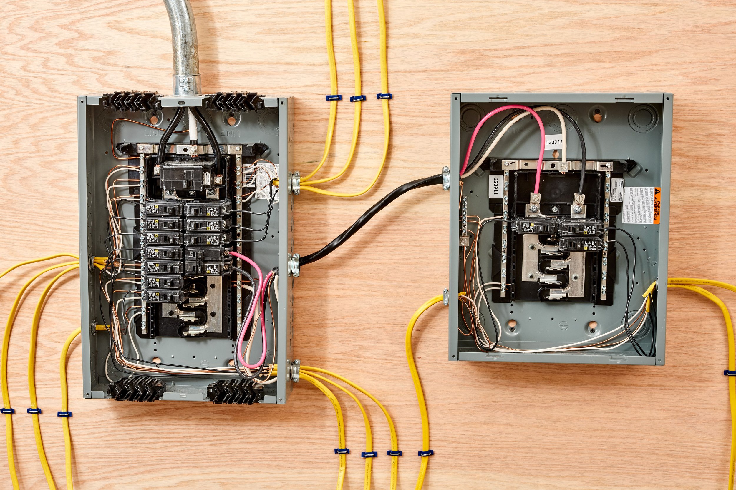 Open electrical breaker panels with wiring inside, placed on a wooden surface.