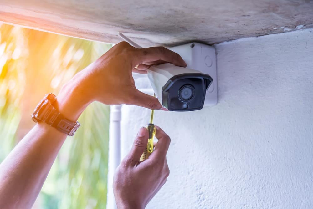 Person installing or maintaining a security camera on an exterior wall using a screwdriver.