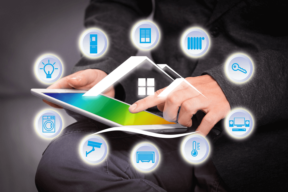 Person in dark clothing using a tablet with smart home technology icons floating around, including a lightbulb, refrigerator, server, radiator, key, washing machine, air conditioner, thermostat, and audio system.