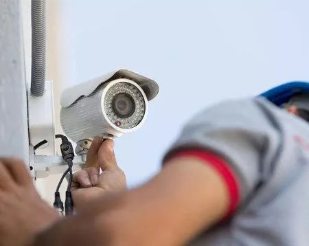 Close-up of a security camera mounted on a wall with a person's arm and hand adjusting it.