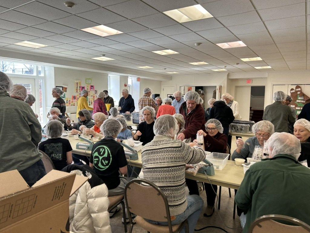 People, including children and seniors, working together at a Rise Against Hunger meal packing event at Wyoming Church