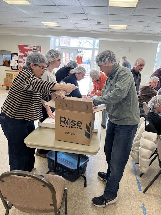 People wearing hairnets packing food into boxes during the Rise Against Hunger meal packing event.