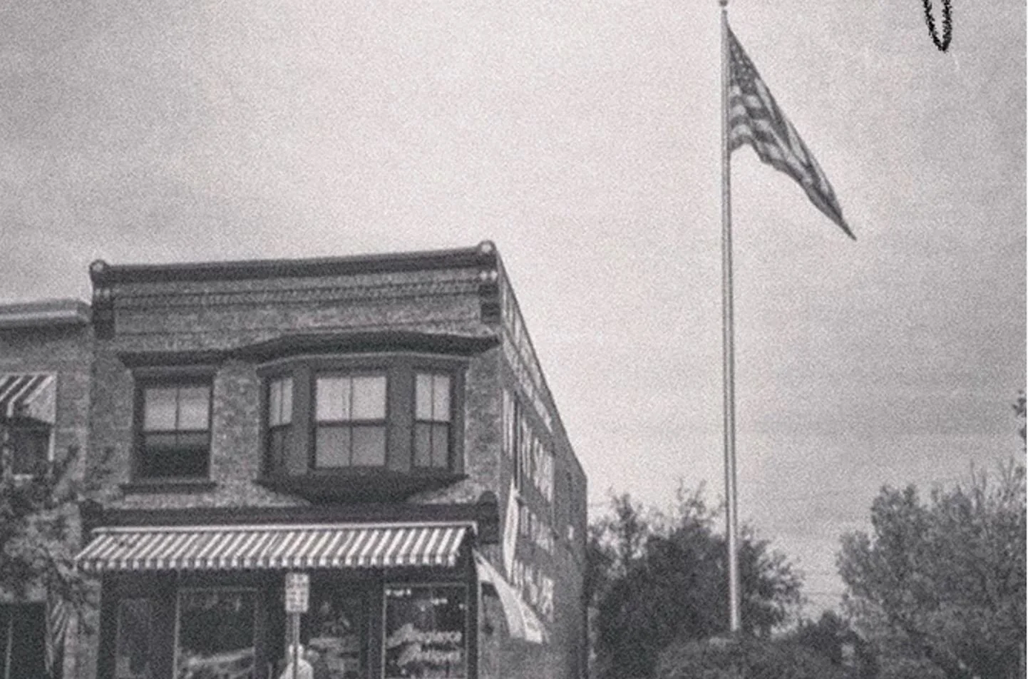 Black and white photo of a brick building with an American flag flying on a tall flagpole nearby.