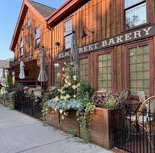 Exterior view of a bakery with wooden and brick facade, flower boxes, and outdoor seating.