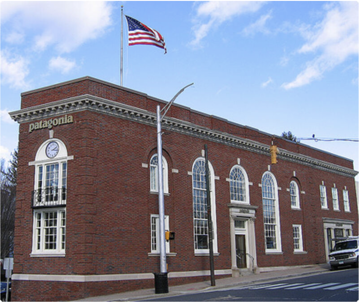 A red brick building with arched windows, a clock, and the word 'patagonia' on the side, topped with an American flag on a flagpole.