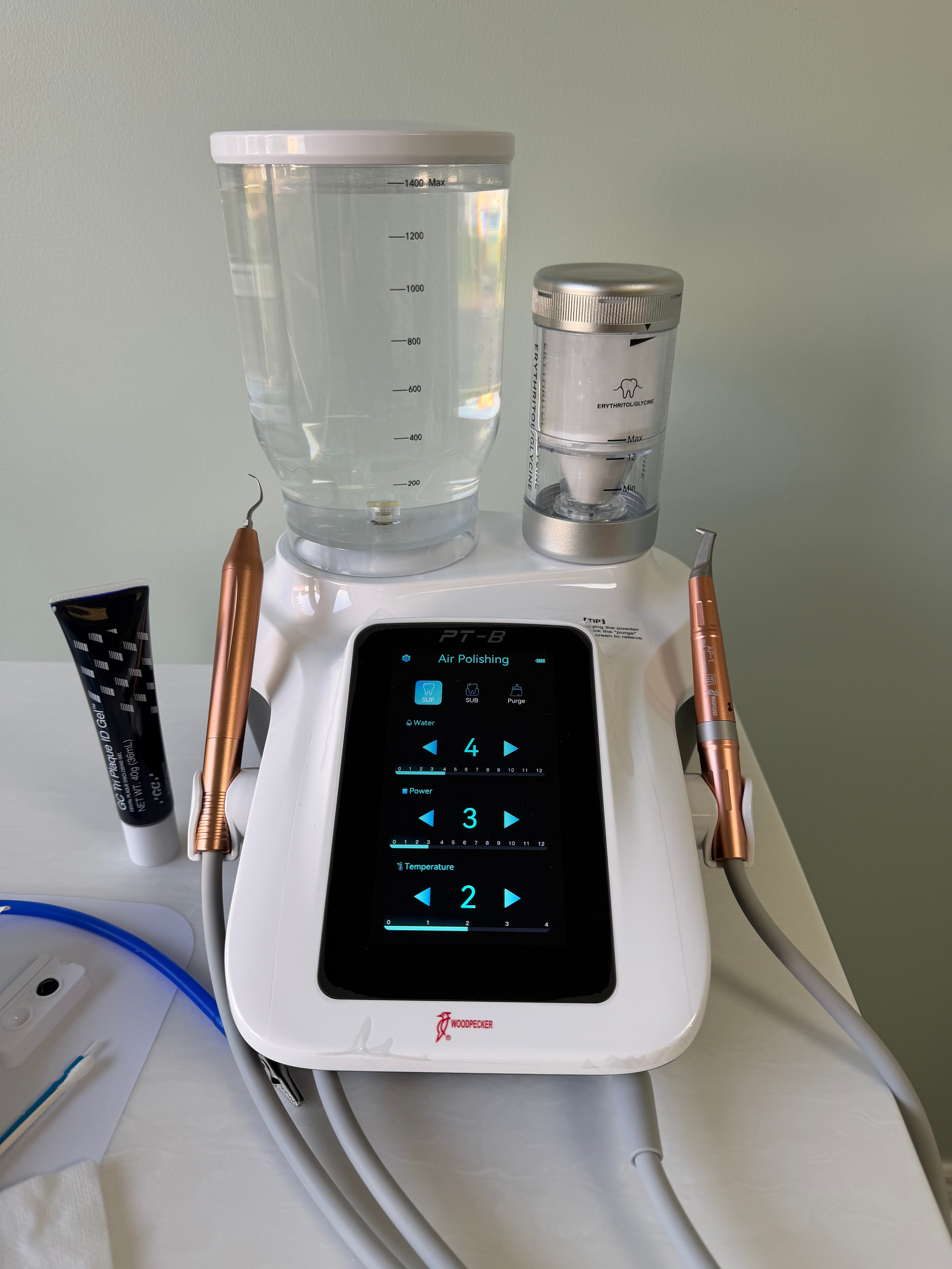 Dental air polisher machine with various dental tools, including a water spray, on a countertop.