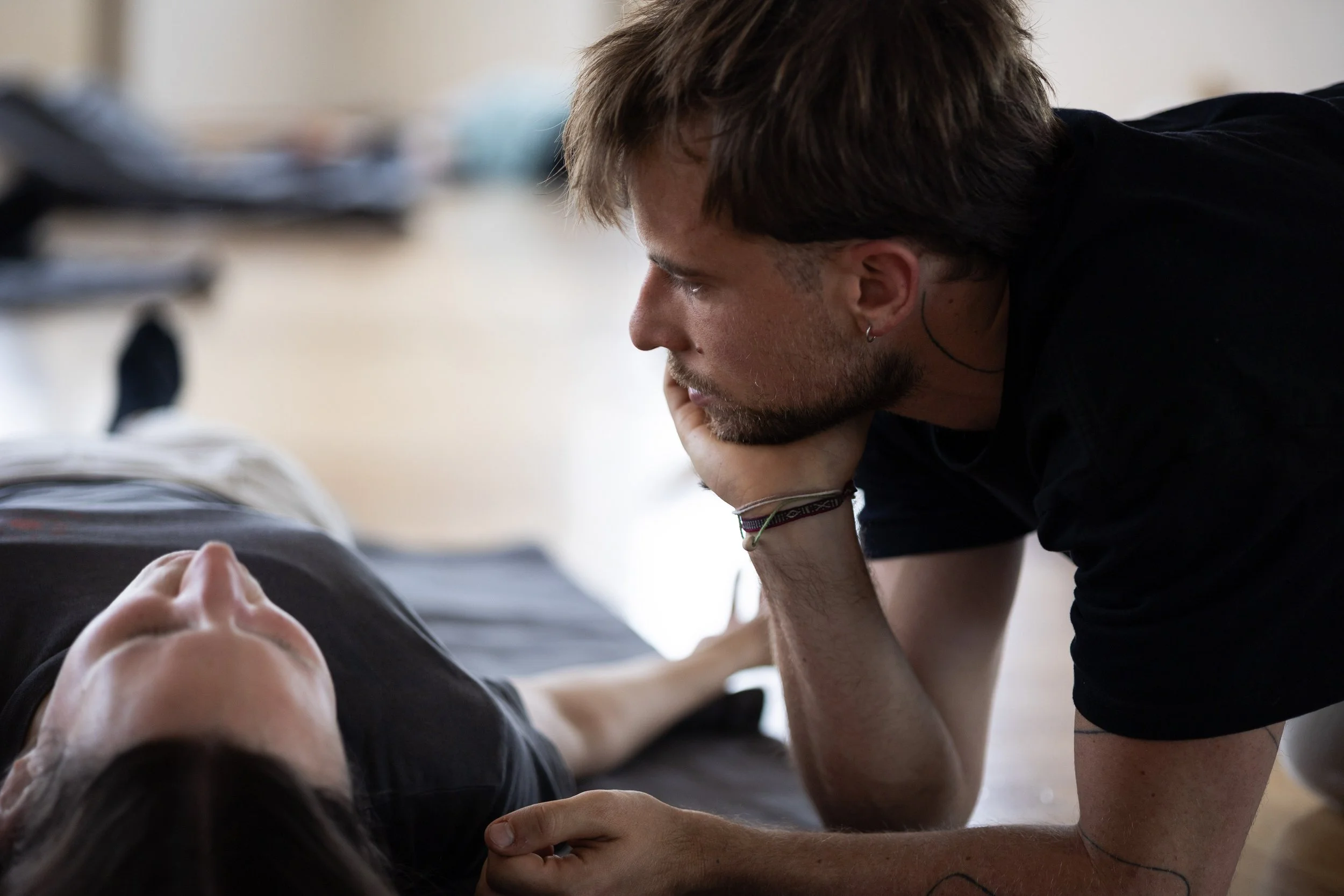 Rouven Dittes, Breathwork Facilitator kniet neben einer liegenden Person und begleitet sie aufmerksam während einer Atemsession