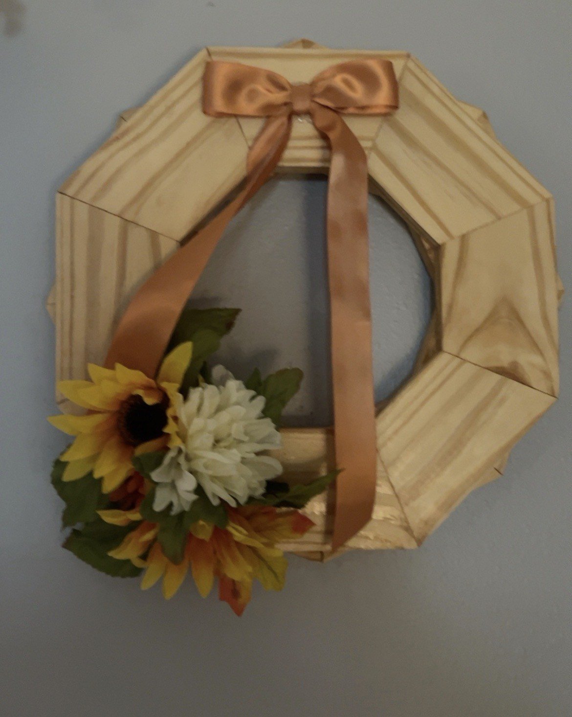 Decorative wooden hexagon-shaped frame with a tan satin bow and artificial sunflower and white flowers