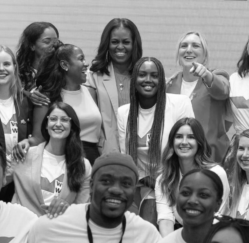 A group of diverse women and one man smiling and posing for a photo at an event.