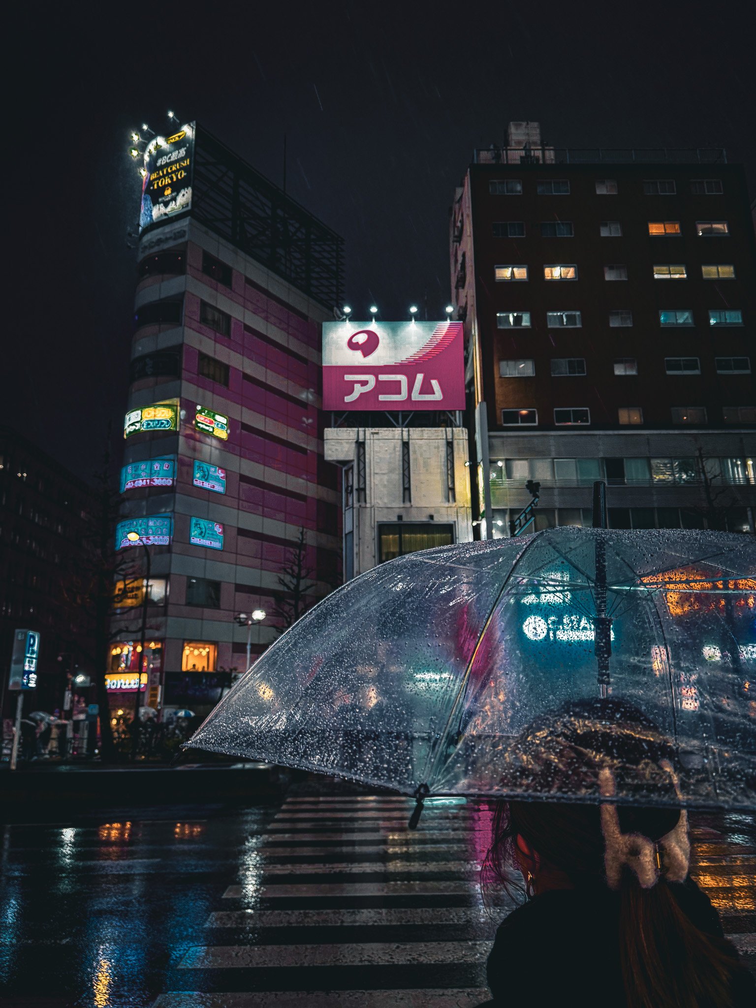 A woman waiting to cross the road at Sukiyabashi Crossing in Ginza Tokyo, looking up at Tsukamoto Sozan Building in the snow, using an umbrella with a cyber punk color edit. 