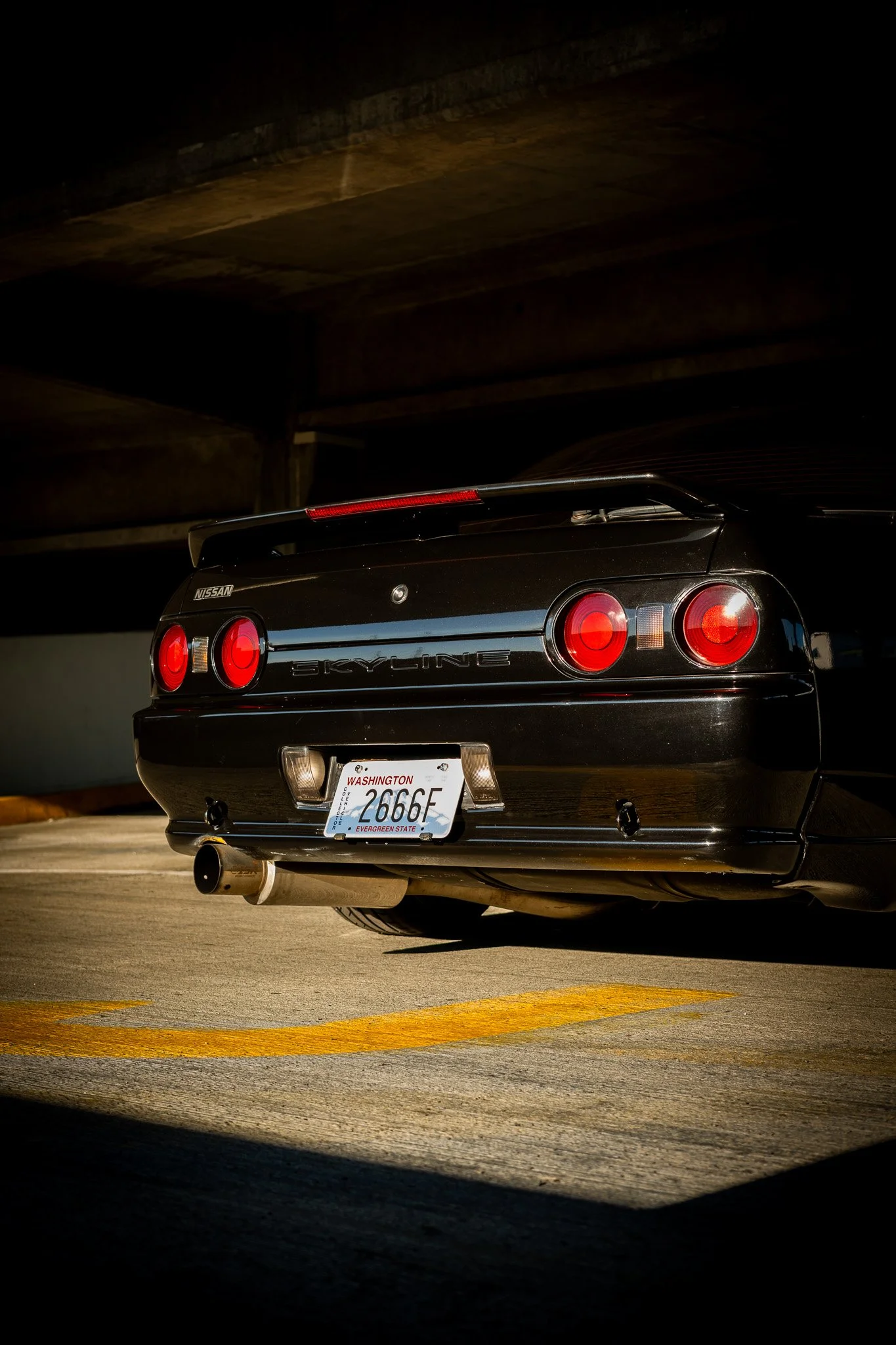 The rear of a black Nissan Skyline car with a Washington license plate, parked in a dimly lit parking garage under a concrete ceiling.