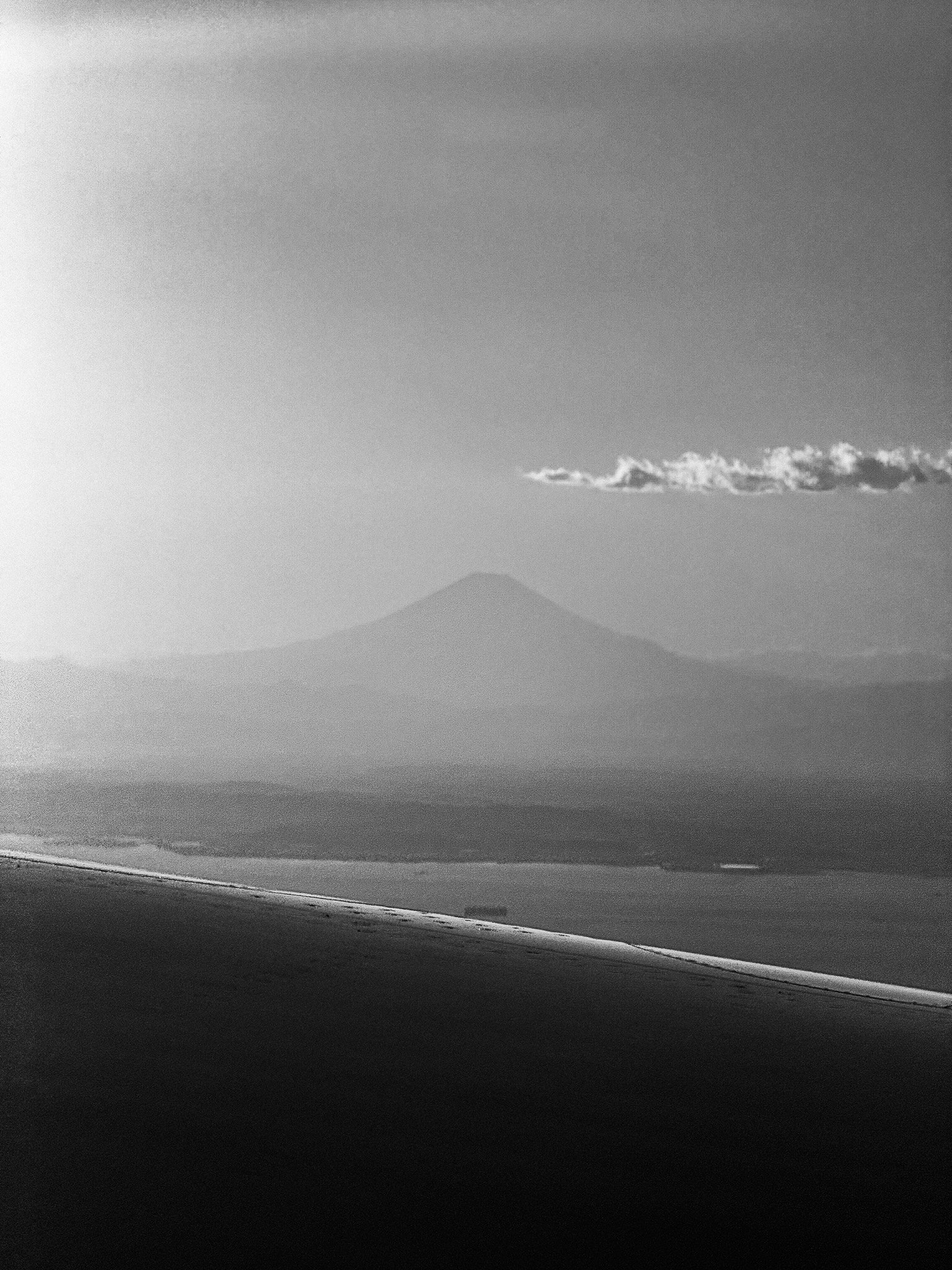 Black and white photograph of a landscape with Mt. Fuji present from an airplane window. 