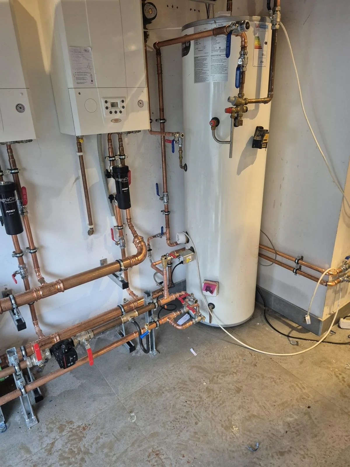 A water heater with multiple copper pipes, shut-off valves, and connected filters in a utility room or basement.