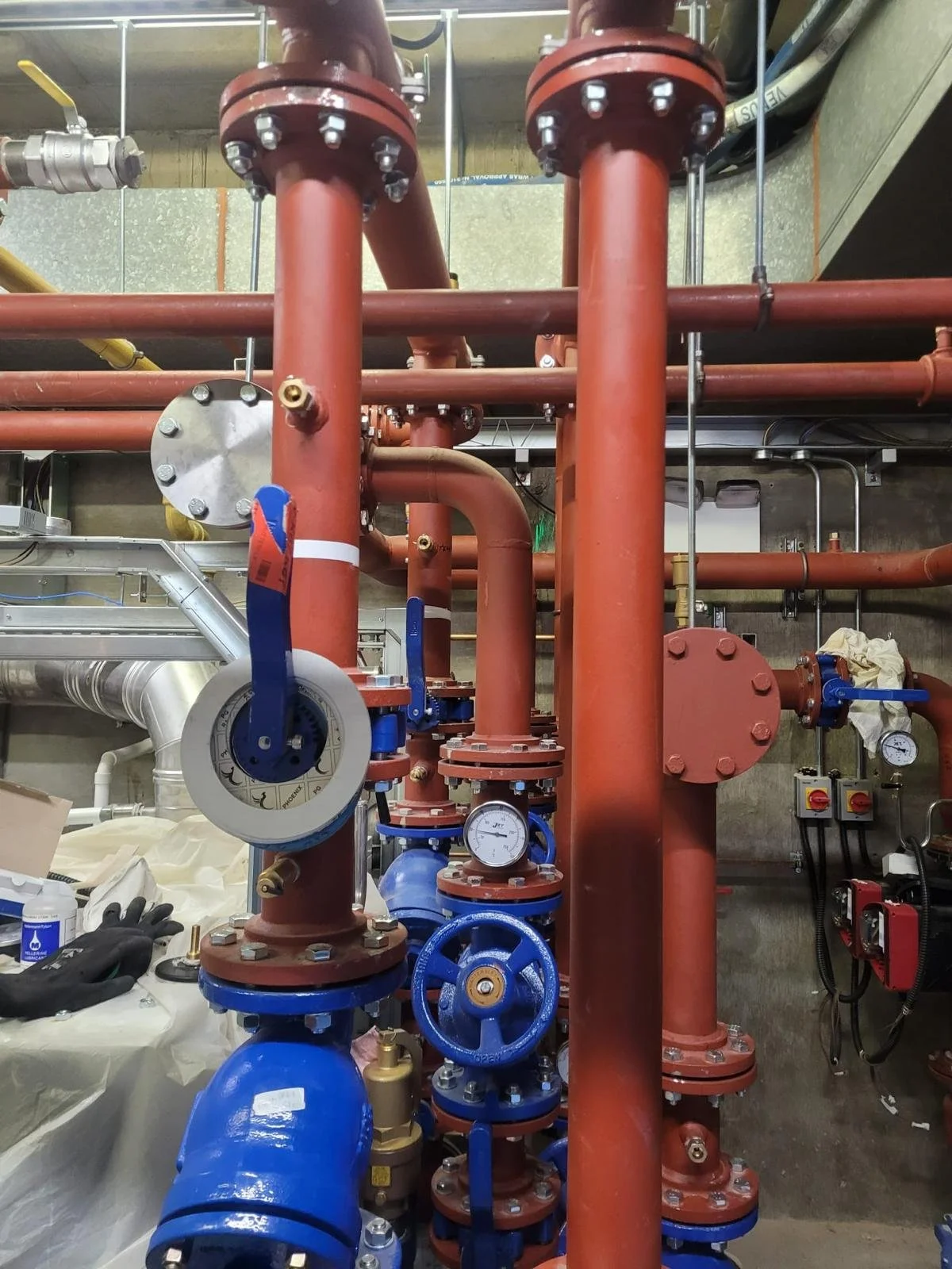 A mechanical room with red and blue pipes, gauges, and valves, indicating a heating or plumbing system installation.