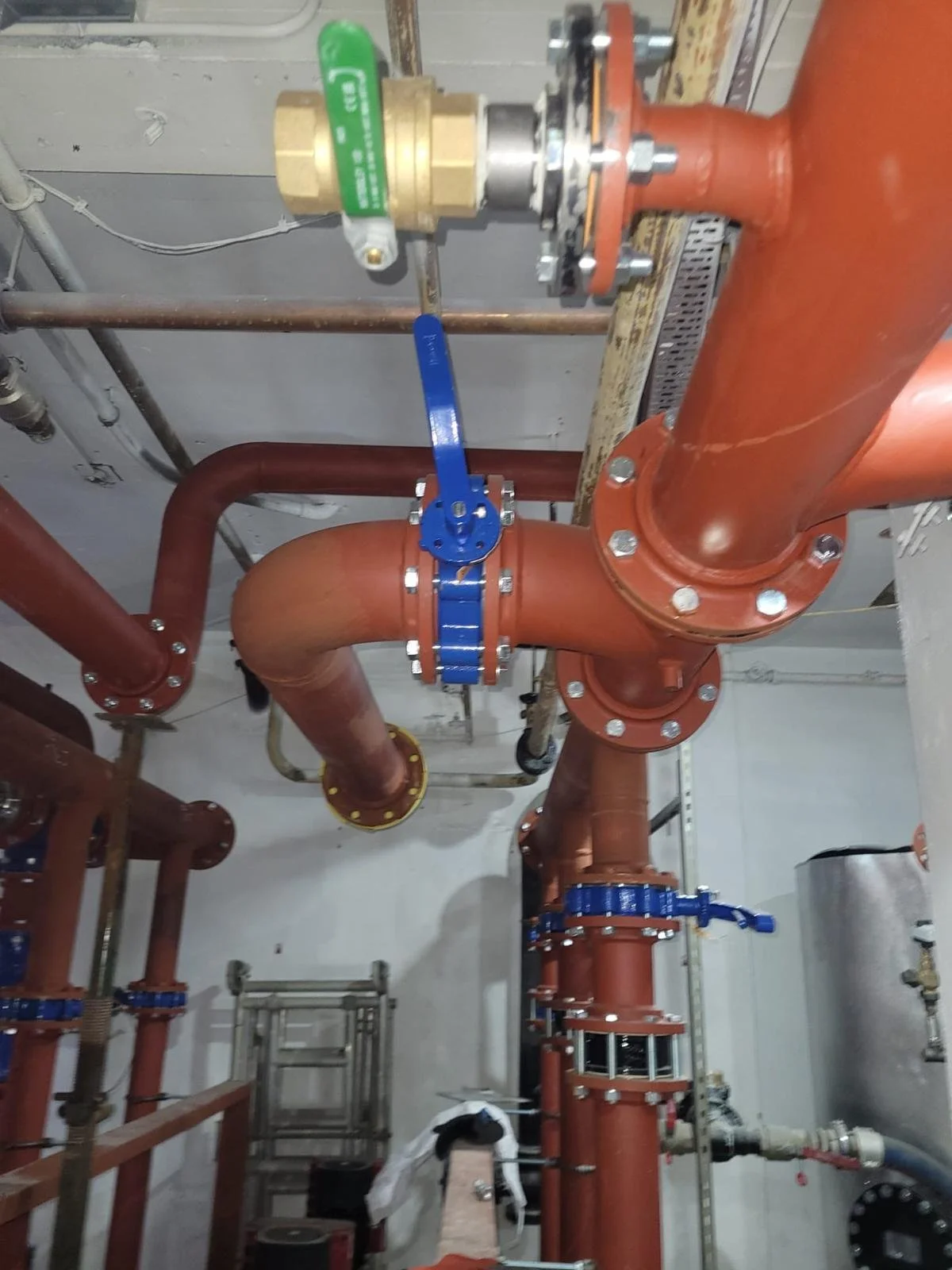 Industrial piping system with large red and bronze pipes, blue valves, and a brass fitting with a green handle.