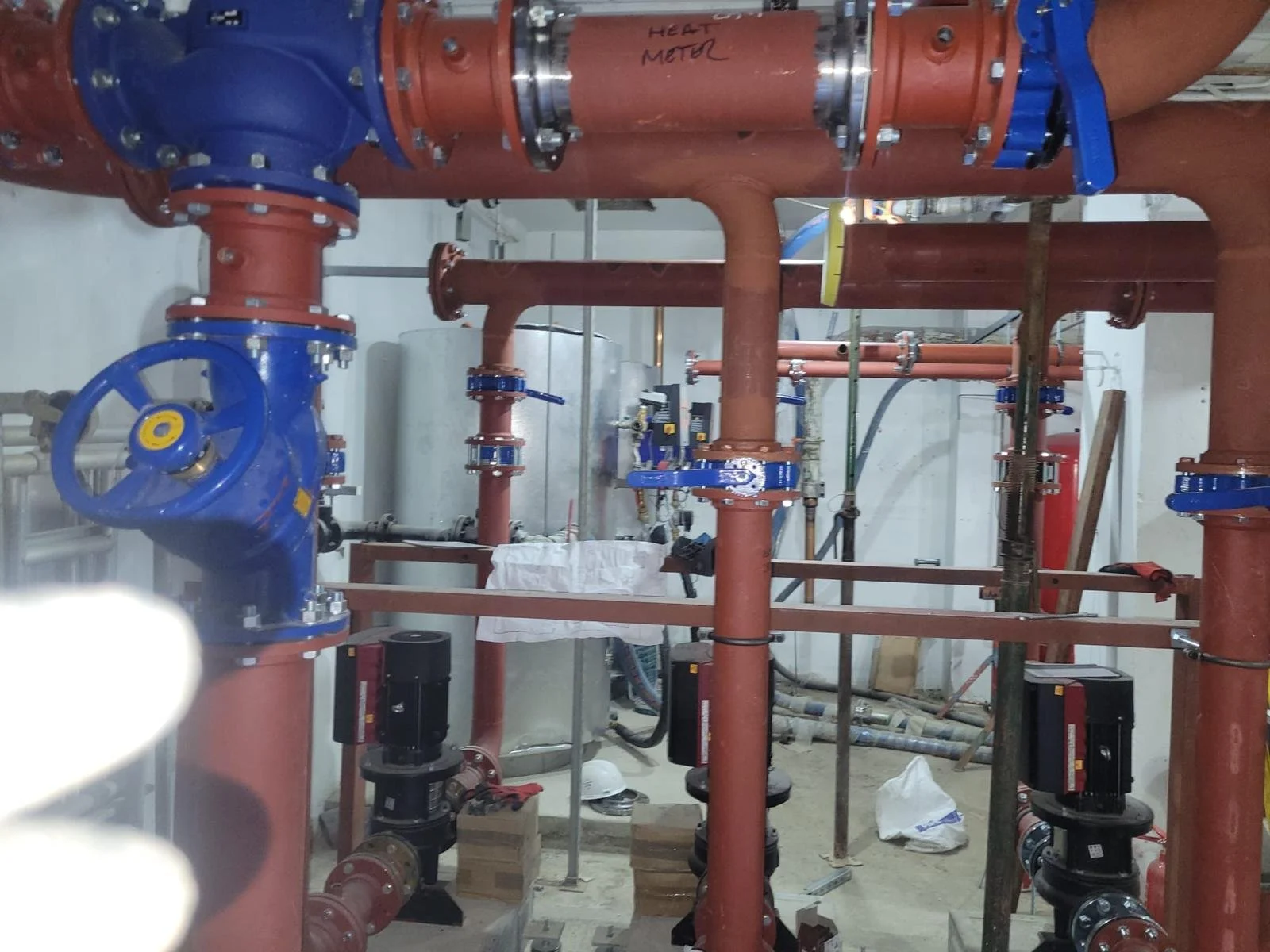 Industrial plumbing system with large red and blue pipes, valves, and fittings in a mechanical room.