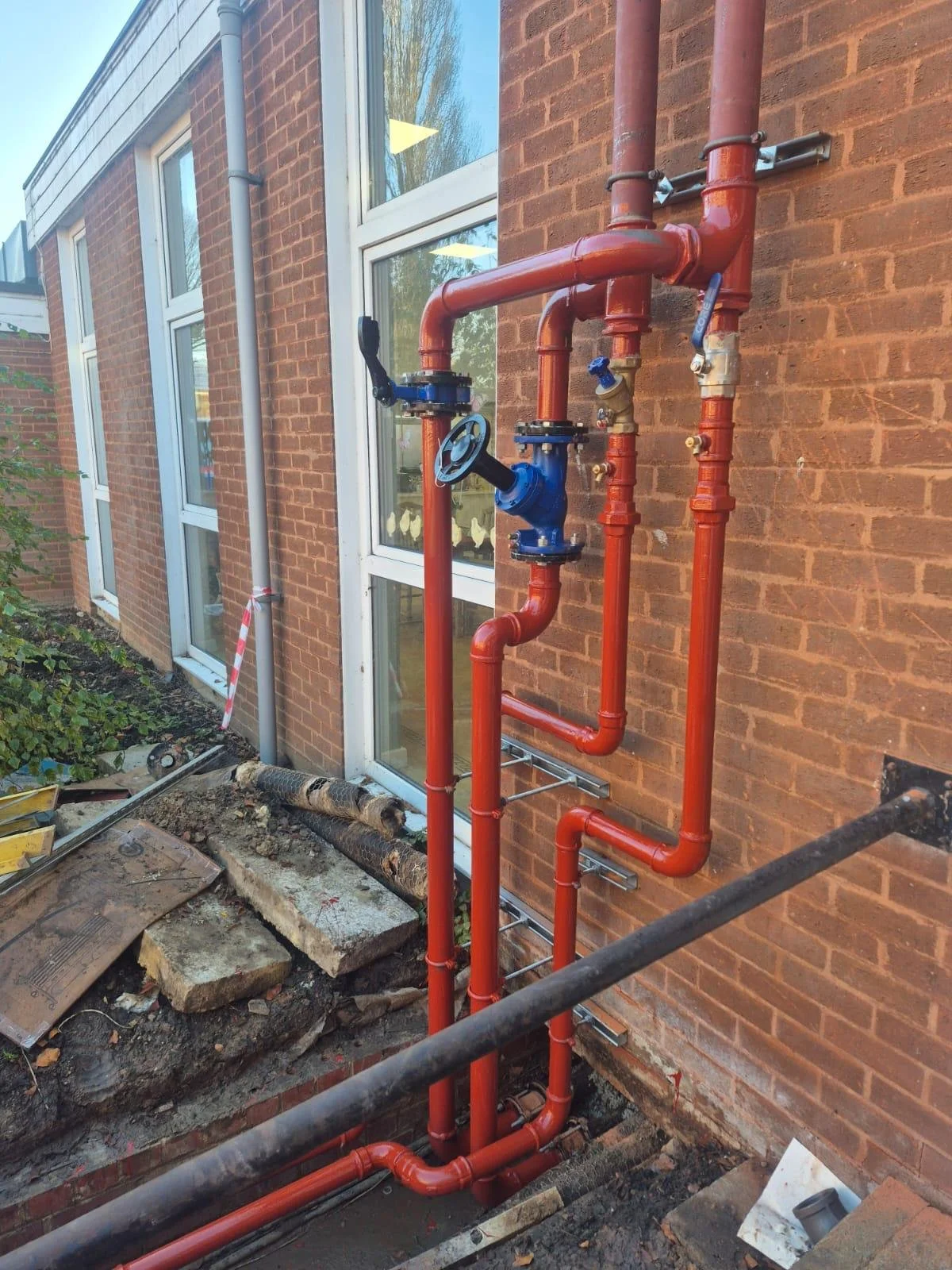 Exterior view of building with red brick wall, white-framed windows, and exposed red plumbing pipes for building utilities.