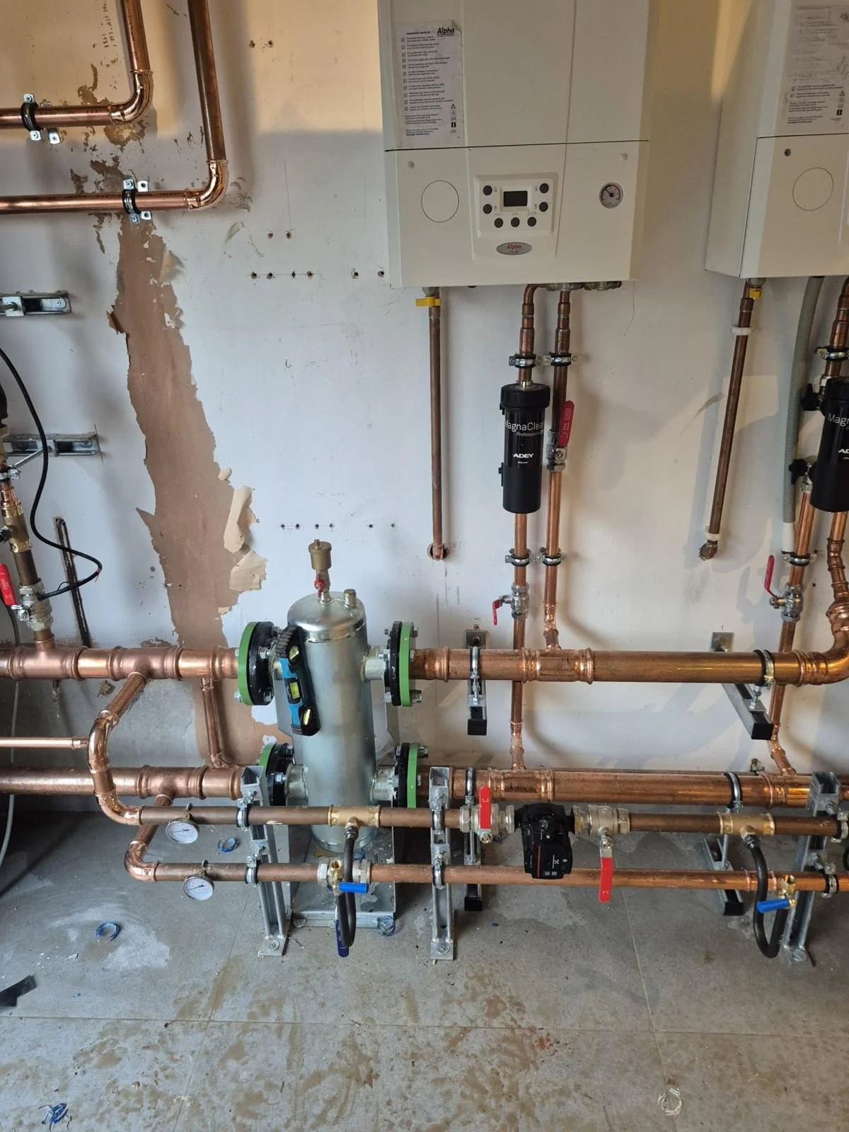 Indoor plumbing and heating system with copper pipes, filters, and control units installed on a wall.