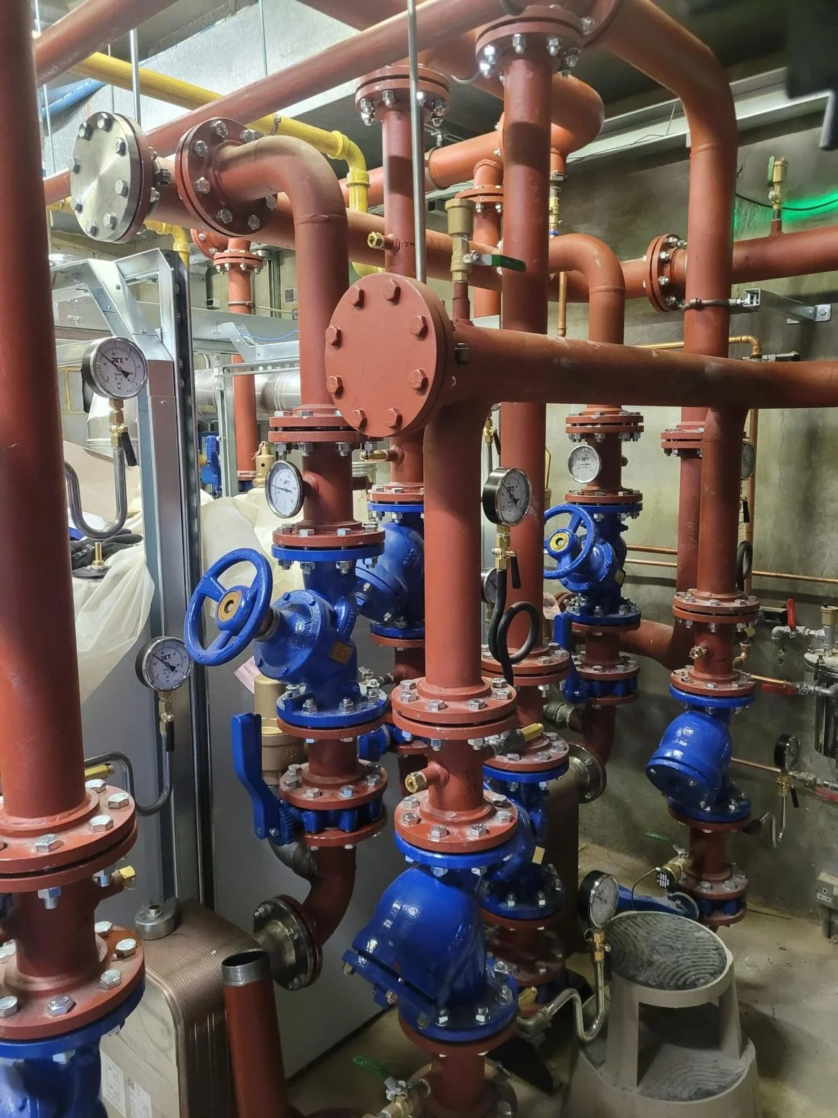 An industrial piping system with brown and blue pipes, gauges, and valves in a mechanical room.