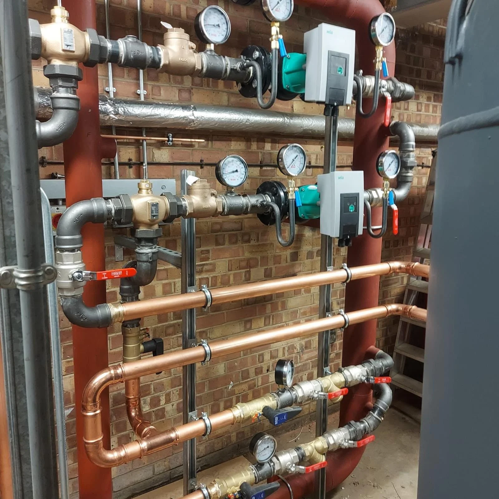 A complex plumbing pipeline system with various pipes, gauges, and valves mounted against a brick wall.