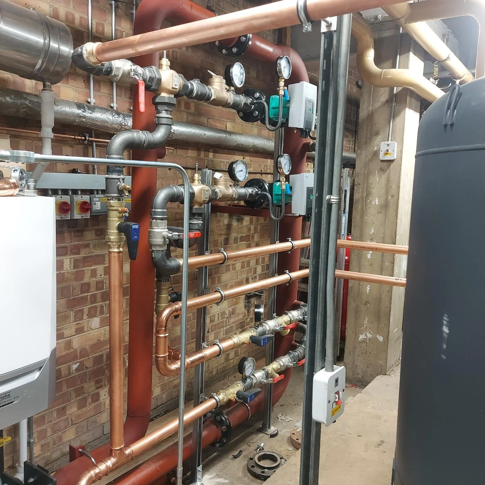 A complex system of plumbing pipes, gauges, and valves installed against a brick wall, likely part of industrial or building heating, cooling, or water systems.