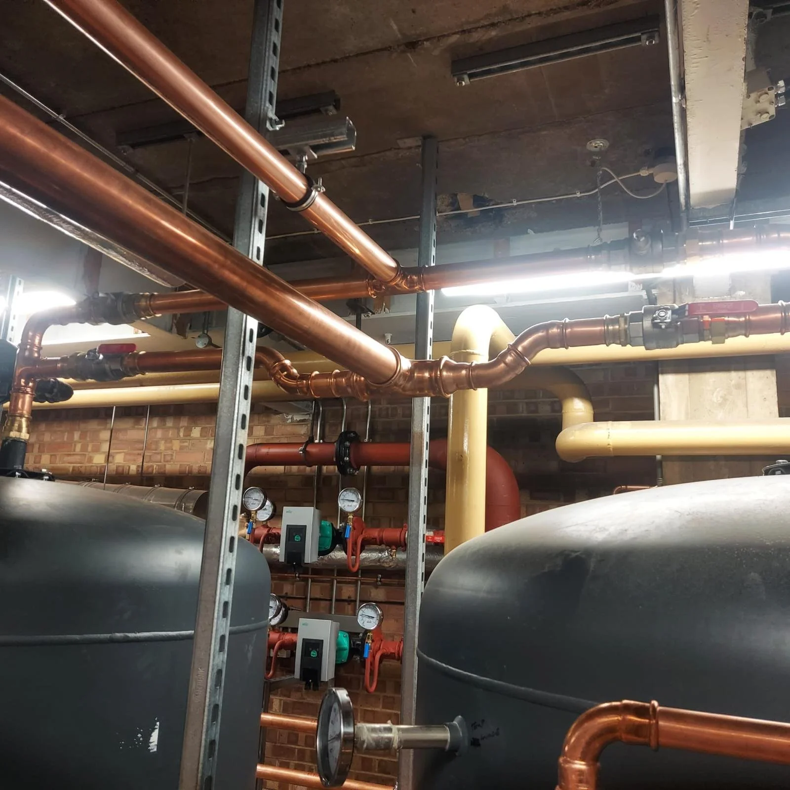 A network of copper and black pipes, valves, and gauges in an industrial or mechanical setting.