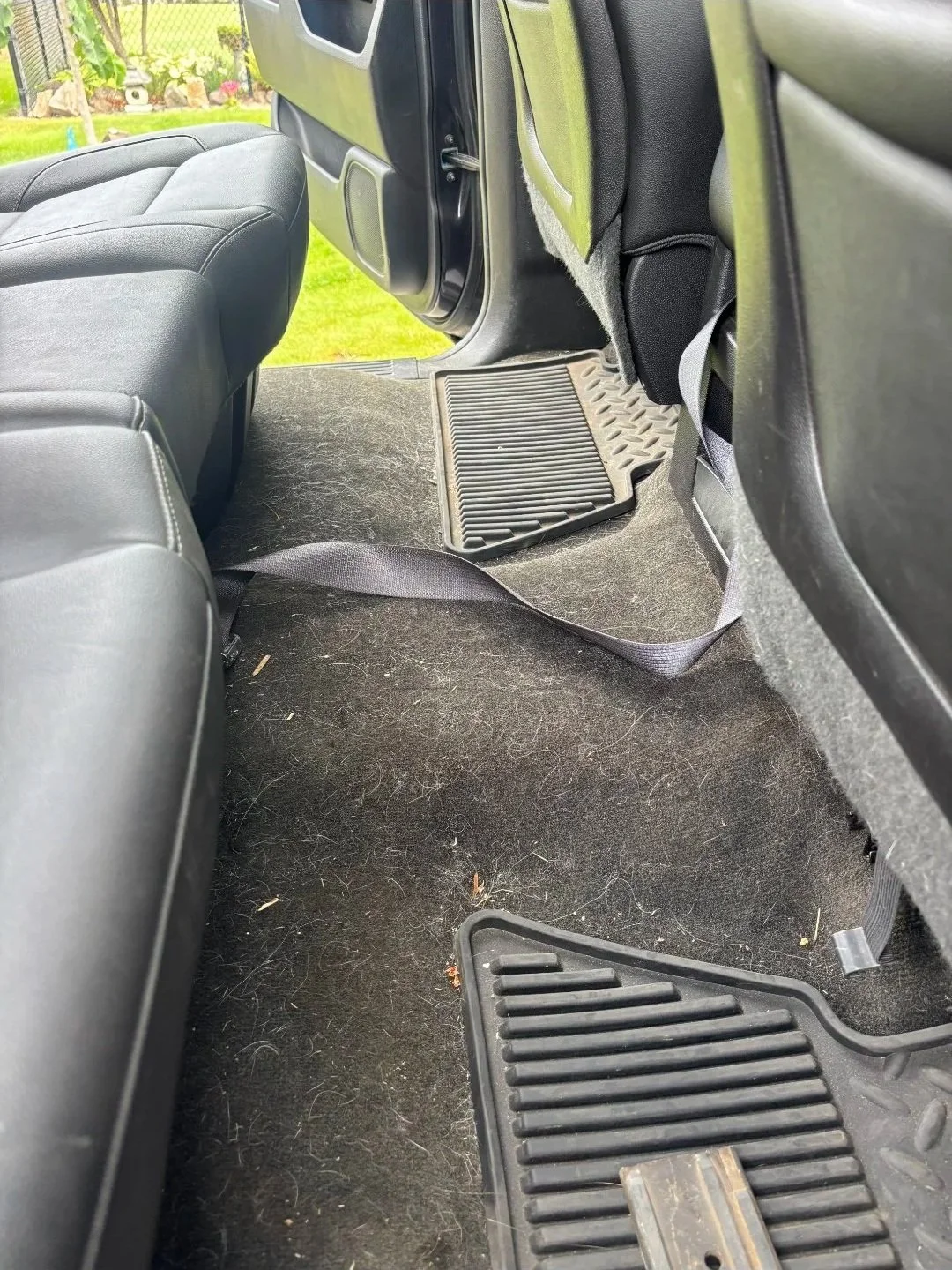 the backseat area of a vehicle showing the floor and floor mats, with some dirt and debris on the carpet.