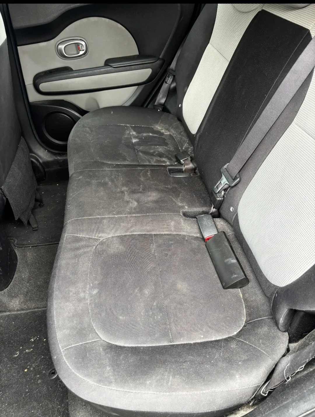 Dirty and dusty fabric car back seat with visible stains and paper scraps.