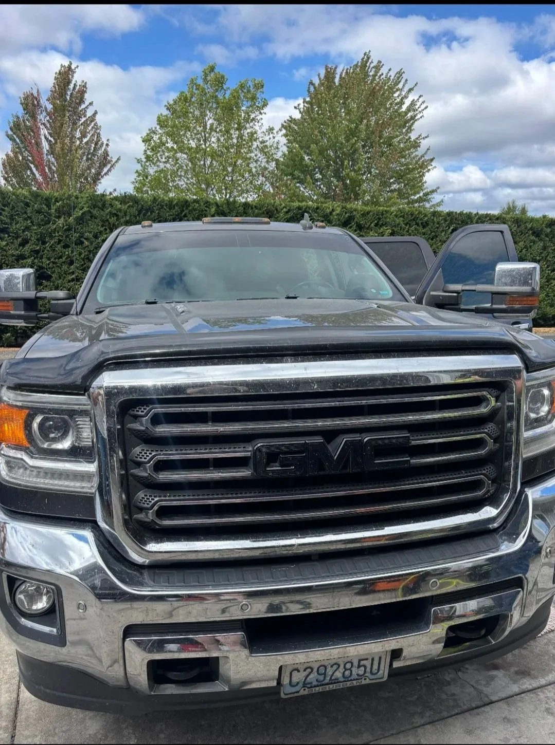 Front view of a black GMC pickup truck with chrome grille and license plate, parked outdoors under cloudy sky with trees in the background.