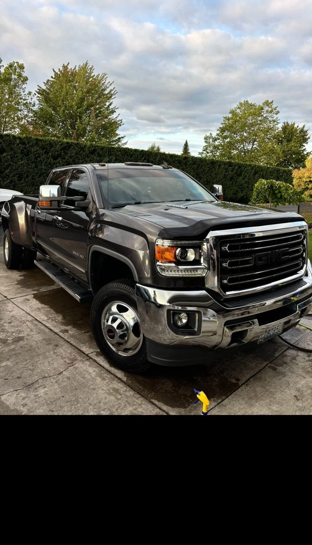 A black GMC Sierra pickup truck parked on a driveway with trees and cloudy sky in the background.