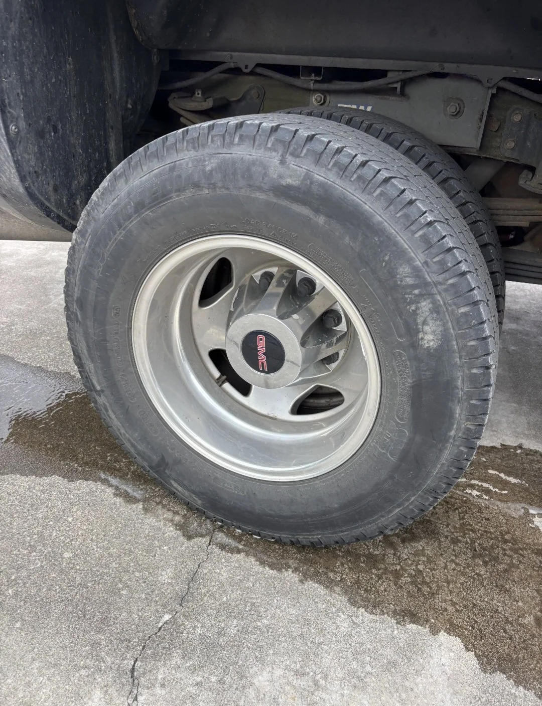 A GMC vehicle tire with a GMC logo on the hubcap, mounted on a concrete surface that appears wet.
