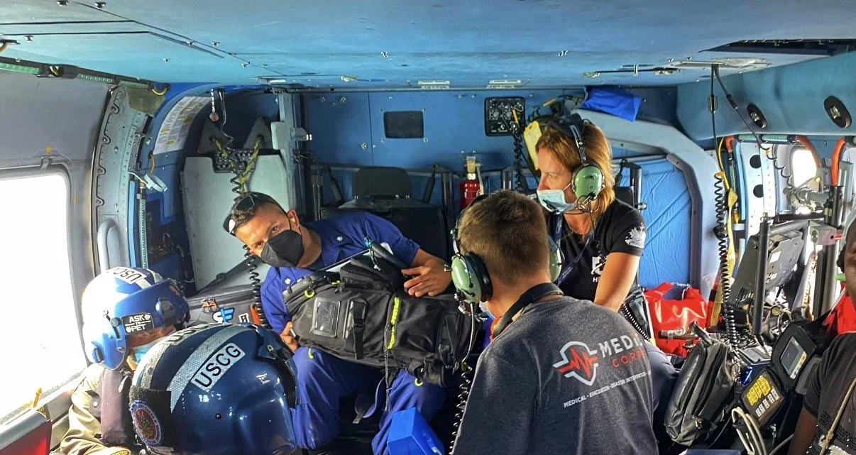 Medical personnel assisting a patient inside an aircraft, with crew members wearing headsets and masks, and a child wearing a firefighter helmet.