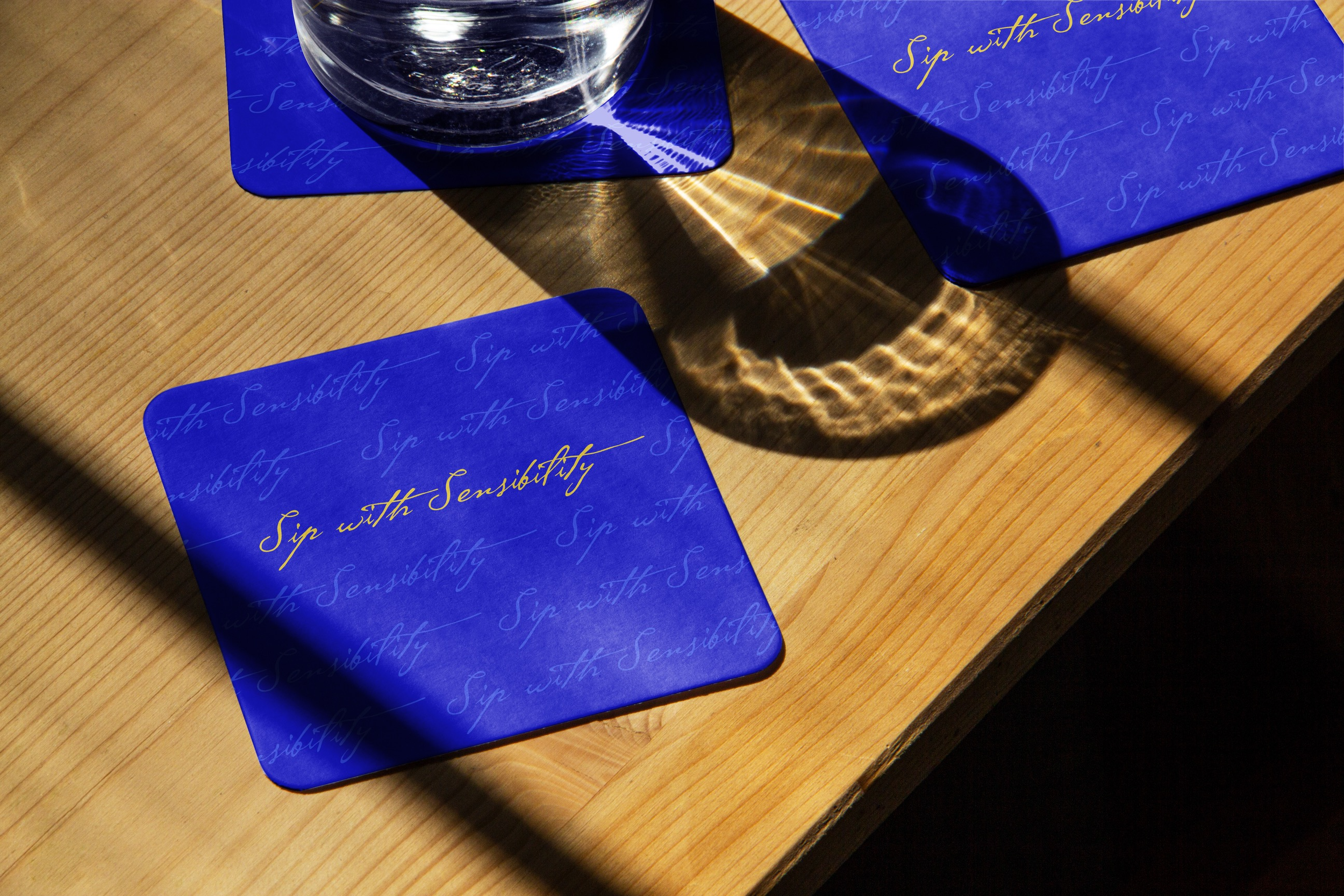 A glass of water cast onto a blue coaster and wooden table, creating a light reflection pattern.