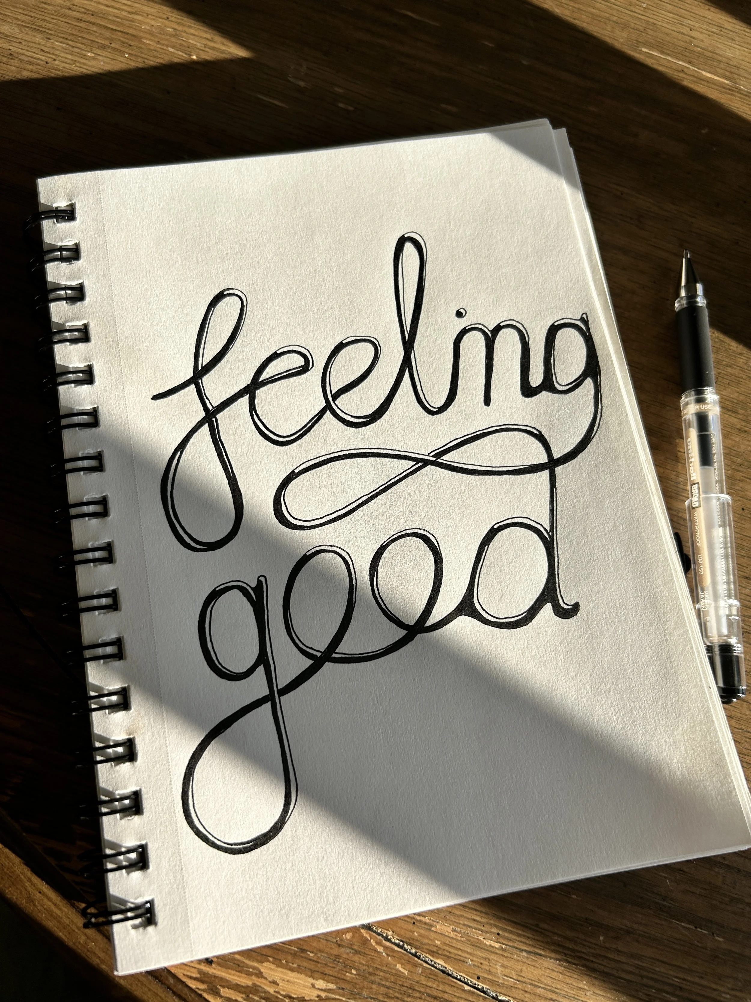 A spiral-bound notebook on a wooden surface with the handwritten words 'hello good' in black marker.