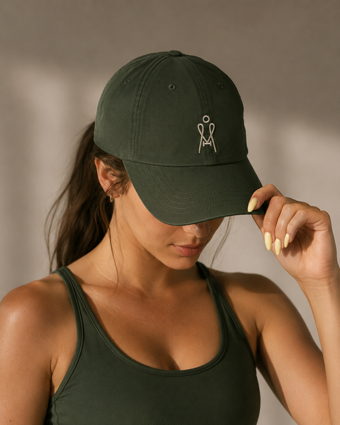 A woman wearing a dark green tank top and matching green cap, with the woman tilting the cap downward, covering her face.
