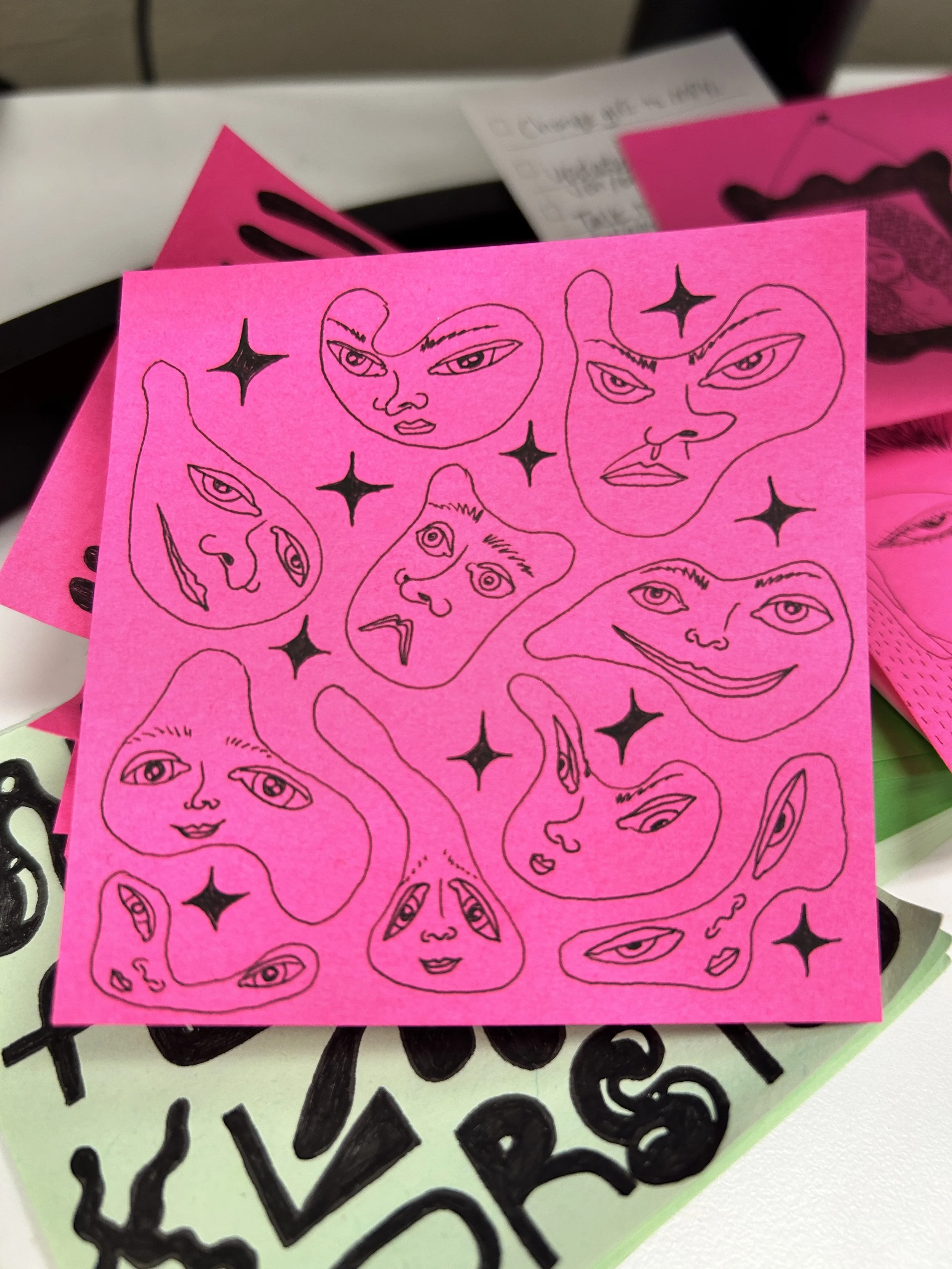 Pink sticky notes with hand-drawn faces and stars, placed on a black and white surface.