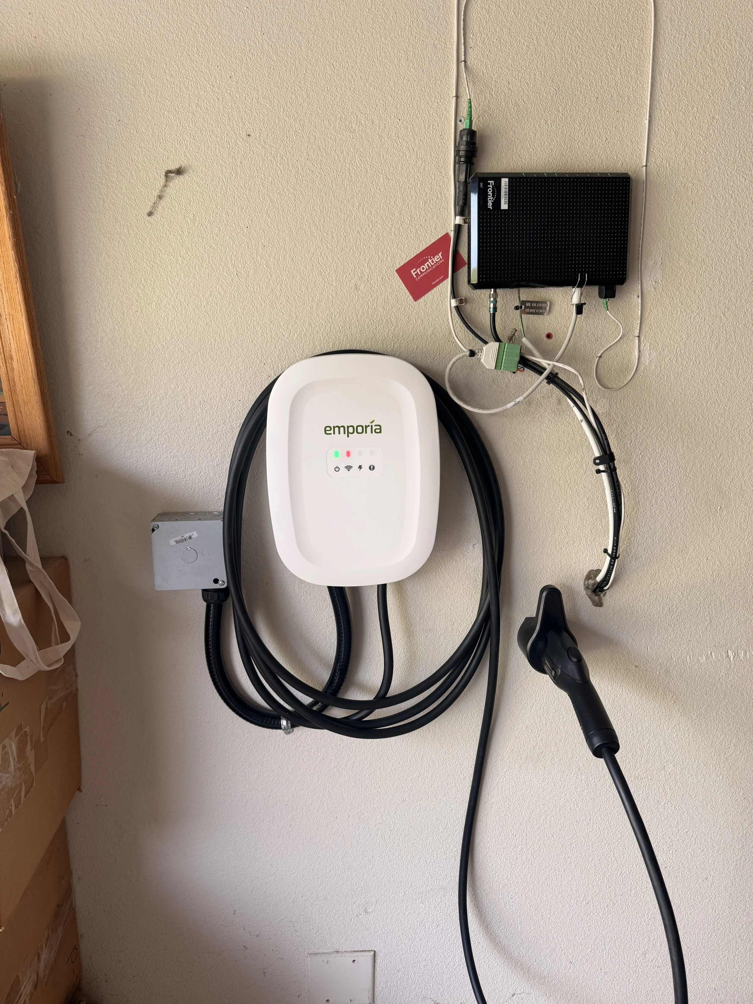 A white wall with an electrical box, an electric vehicle charging station labeled 'emporia', and a black charging cable connected to a charging connector.