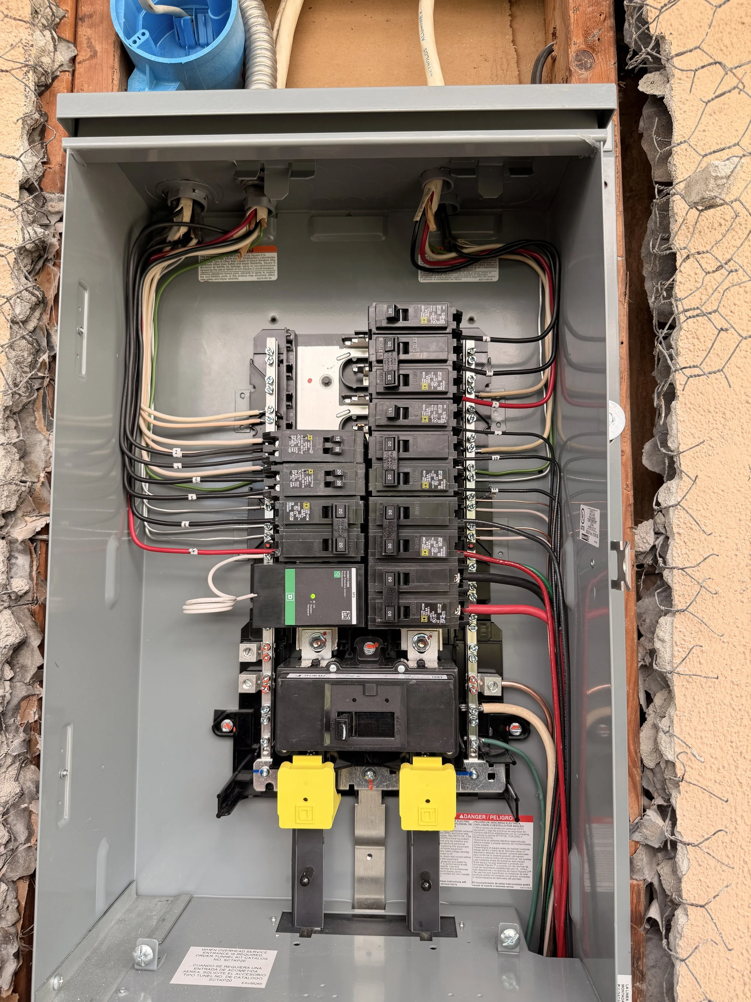 An open electrical panel with circuit breakers and wiring inside a metal box, mounted outdoors on a brick wall.