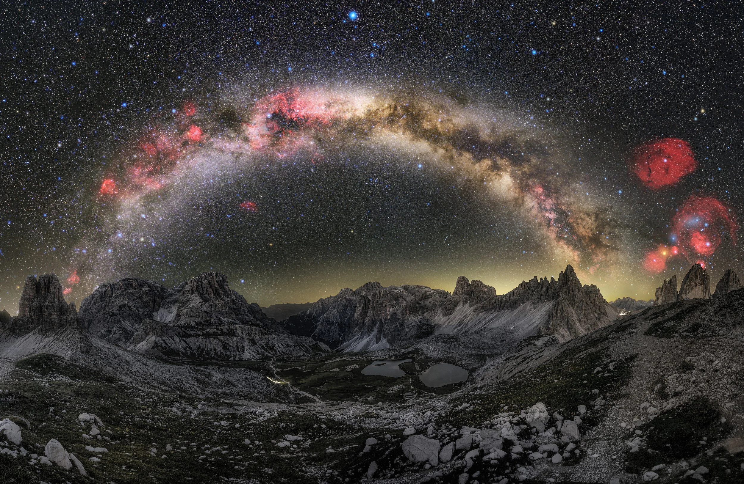 Night sky filled with stars and the Milky Way galaxy over a rugged mountain landscape with snow patches and rocky terrain.